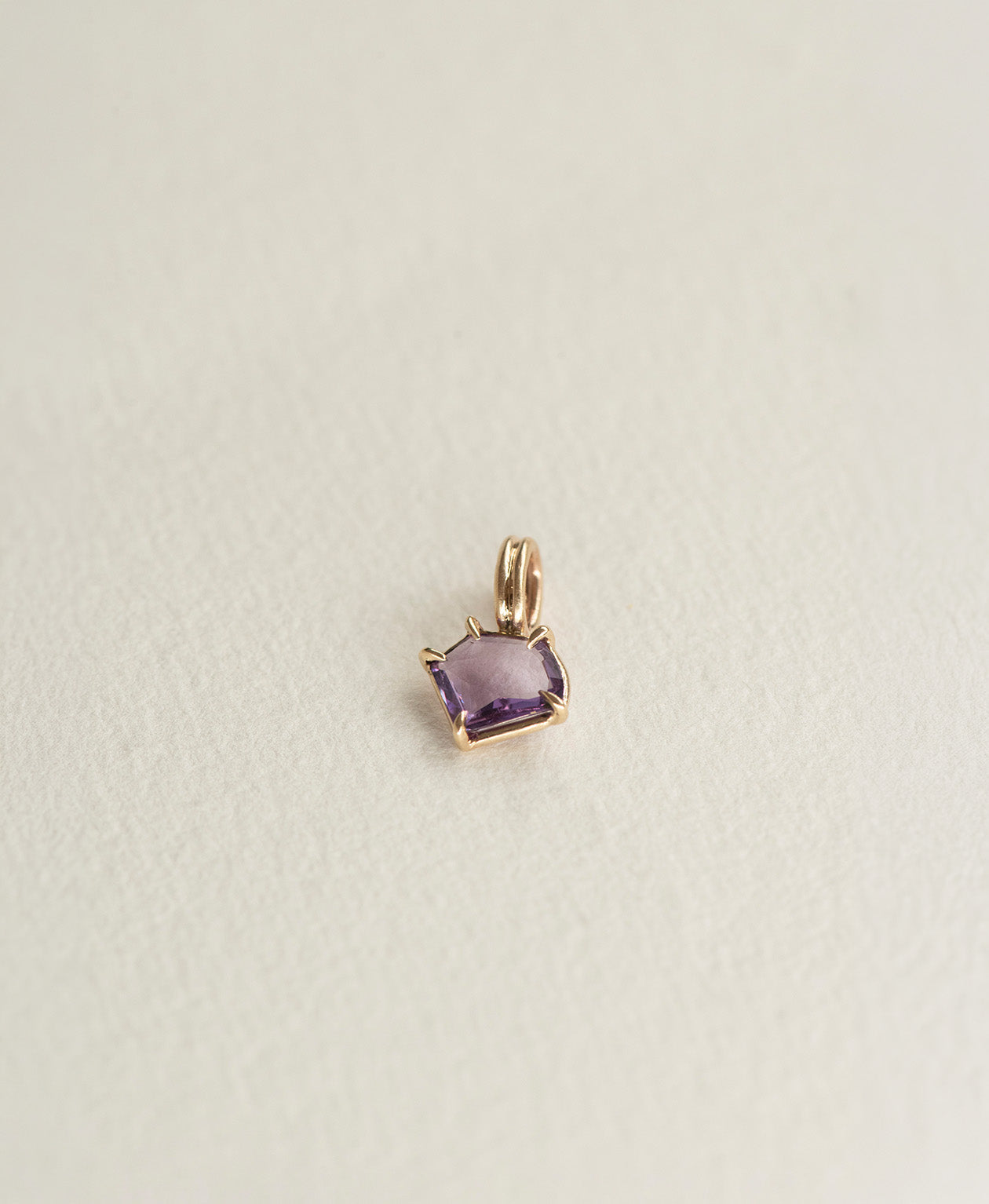 Angled view of the One of a Kind Charm 495 in 9k Yellow Gold with a portrait cut purple sapphire.