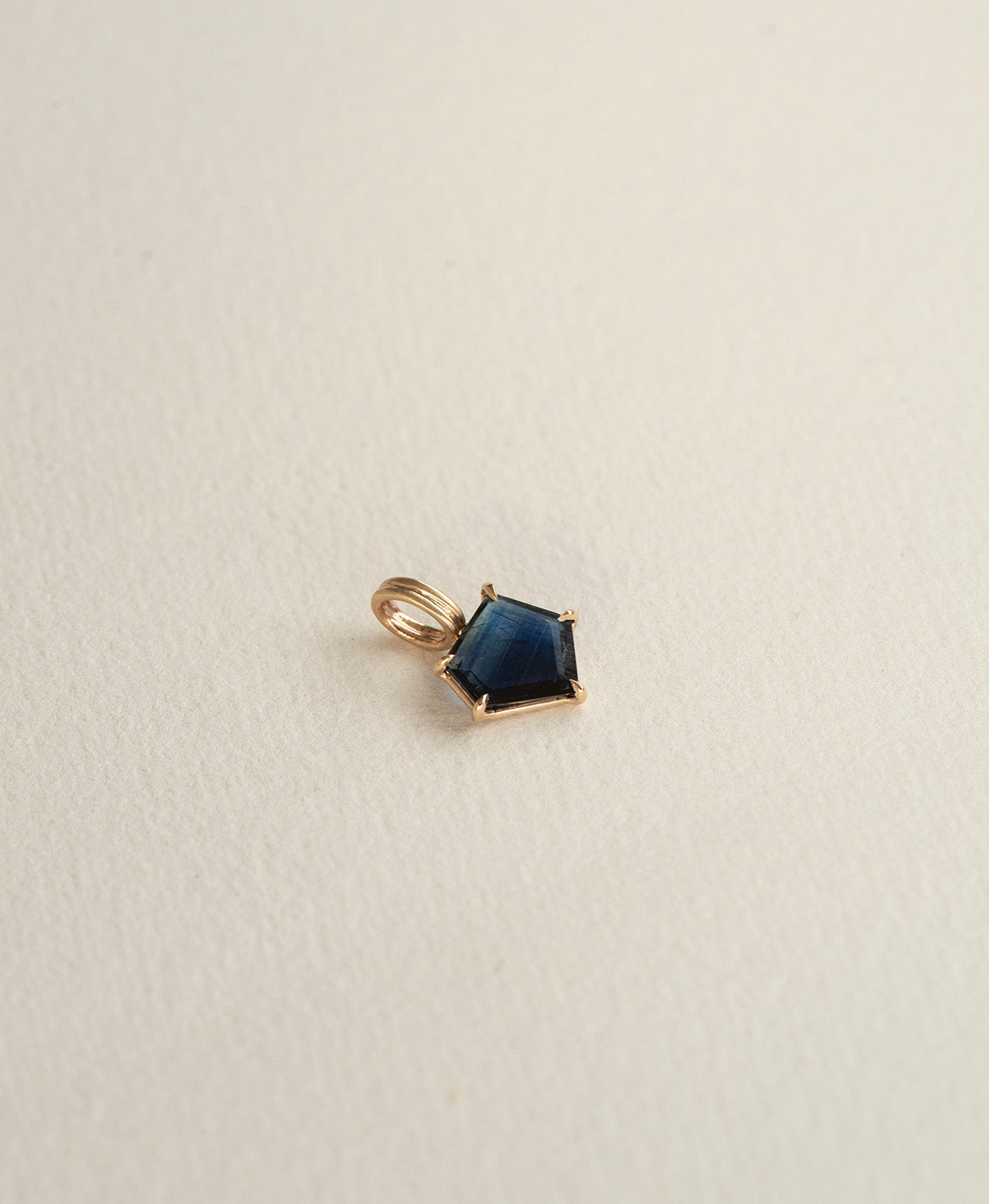 Angled view of the One of a Kind Charm 508 in 9k Yellow Gold with a deep blue portrait cut Sapphire.