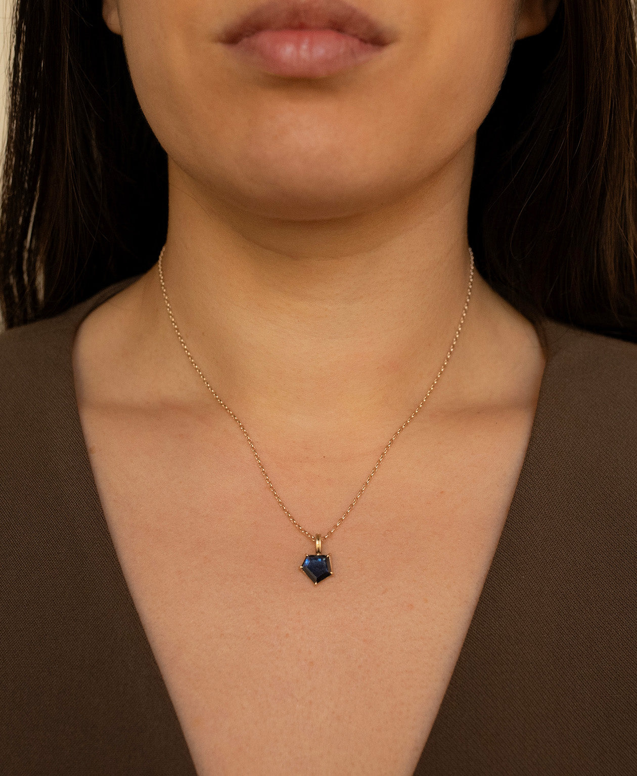 Close up of the One of a Kind Charm 508 with a deep blue portrait cut Sapphire worn by a model on a fine belcher chain.