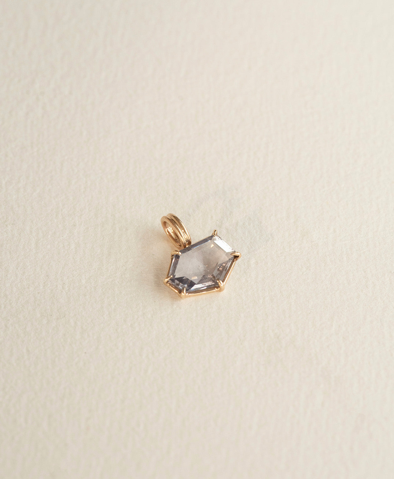 Angled view of the One of a Kind Charm 509 in 9k Yellow Gold with a lilac hexagonal cut Sapphire.