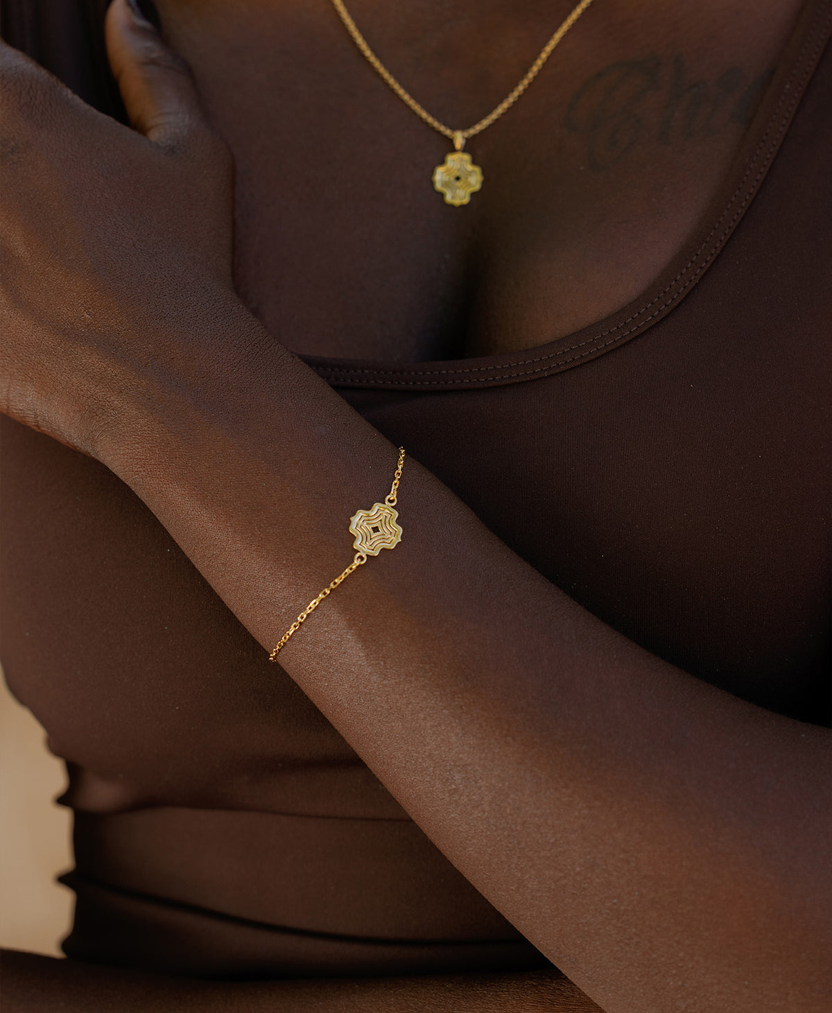 A close-up of a wrist wearing the Alma Bracelet, a gold pendant with a concentric wave design set on a fine cable chain.