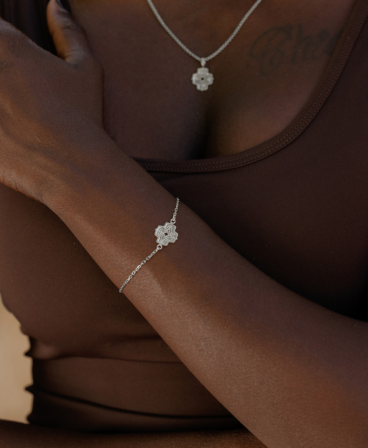A close-up of a wrist wearing the Alma Bracelet, a silver pendant with a concentric wave design set on a fine cable chain.