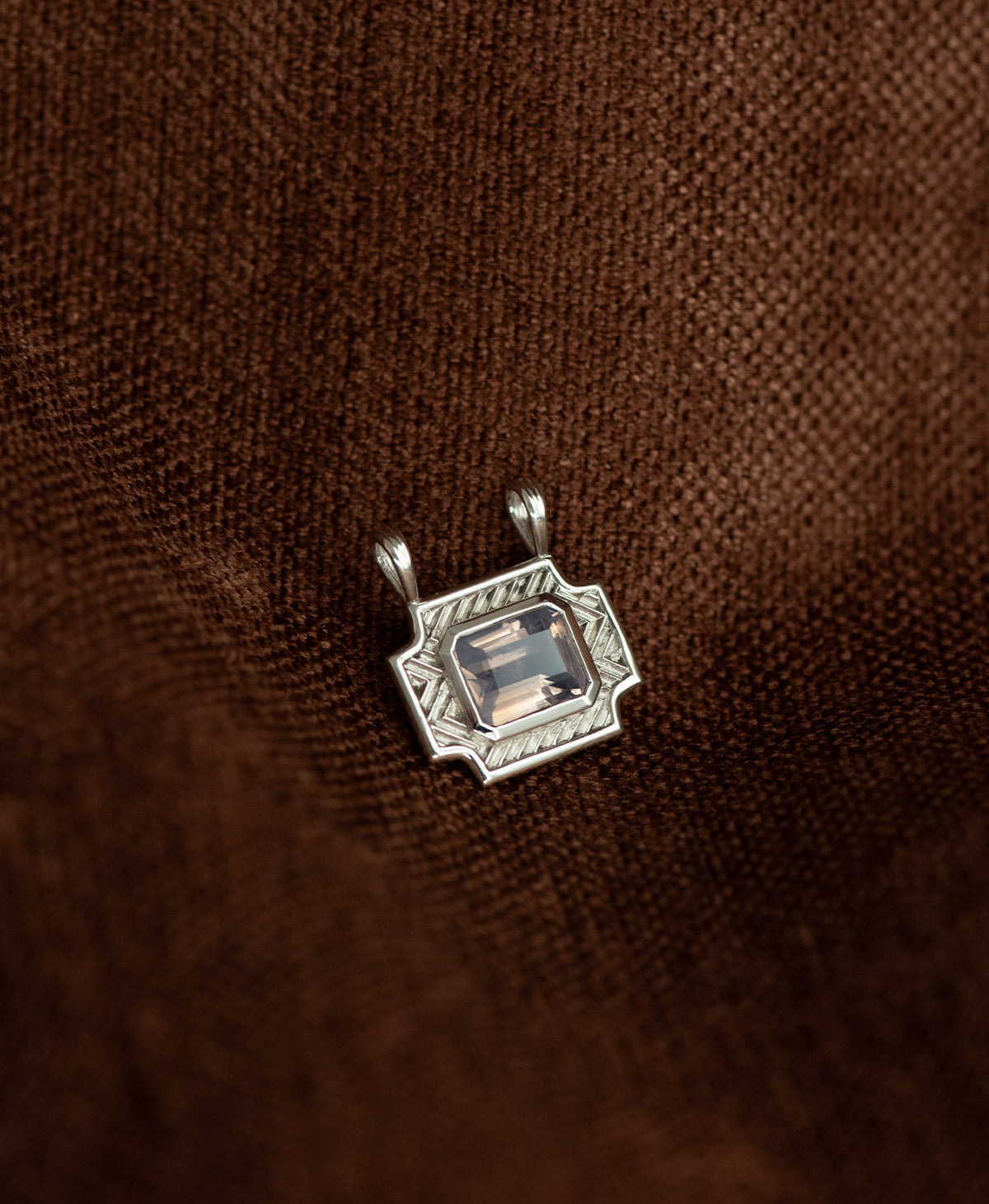 A silver pendant with a rectangular lavender quartz stone, resting against a textured brown background.