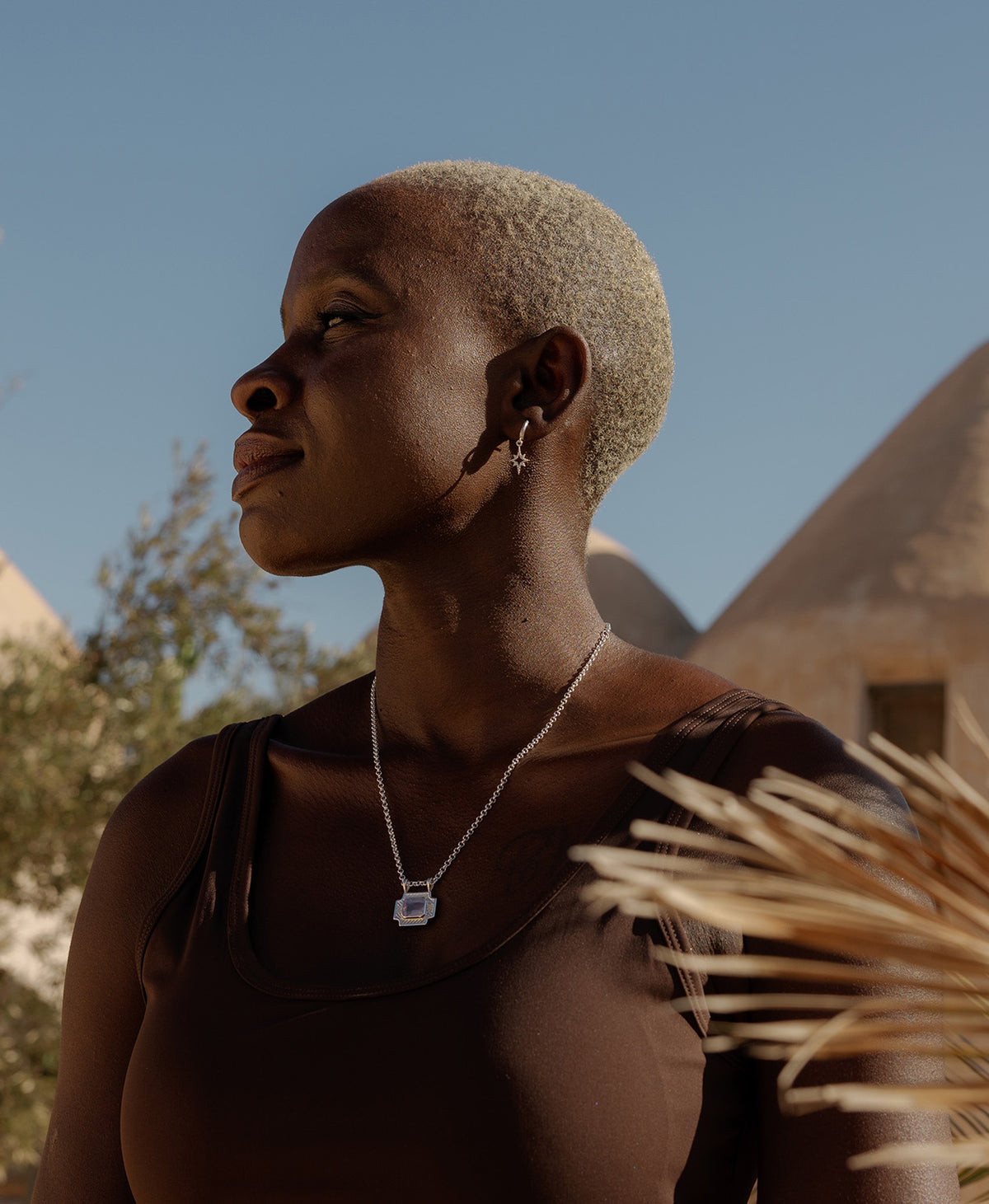 A person wearing the Ayla charm, a silver textured rectangular pendant with a central lavender stone, paired with a belcher chain and silver star earrings.