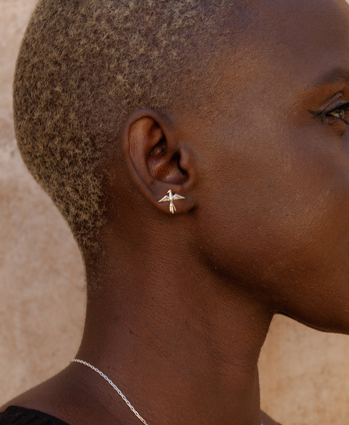 A close-up side profile of a person wearing the silver Bird of a Feather Studs, featuring a bird stud earrings with detailed feather and wing textures.