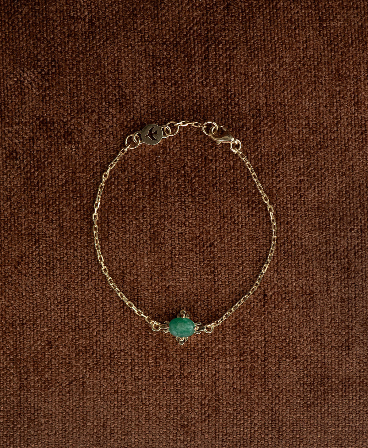 The gold Farah Bracelet featuring a cabochon cut emerald, layered over a cream stone on a textured brown fabric background.