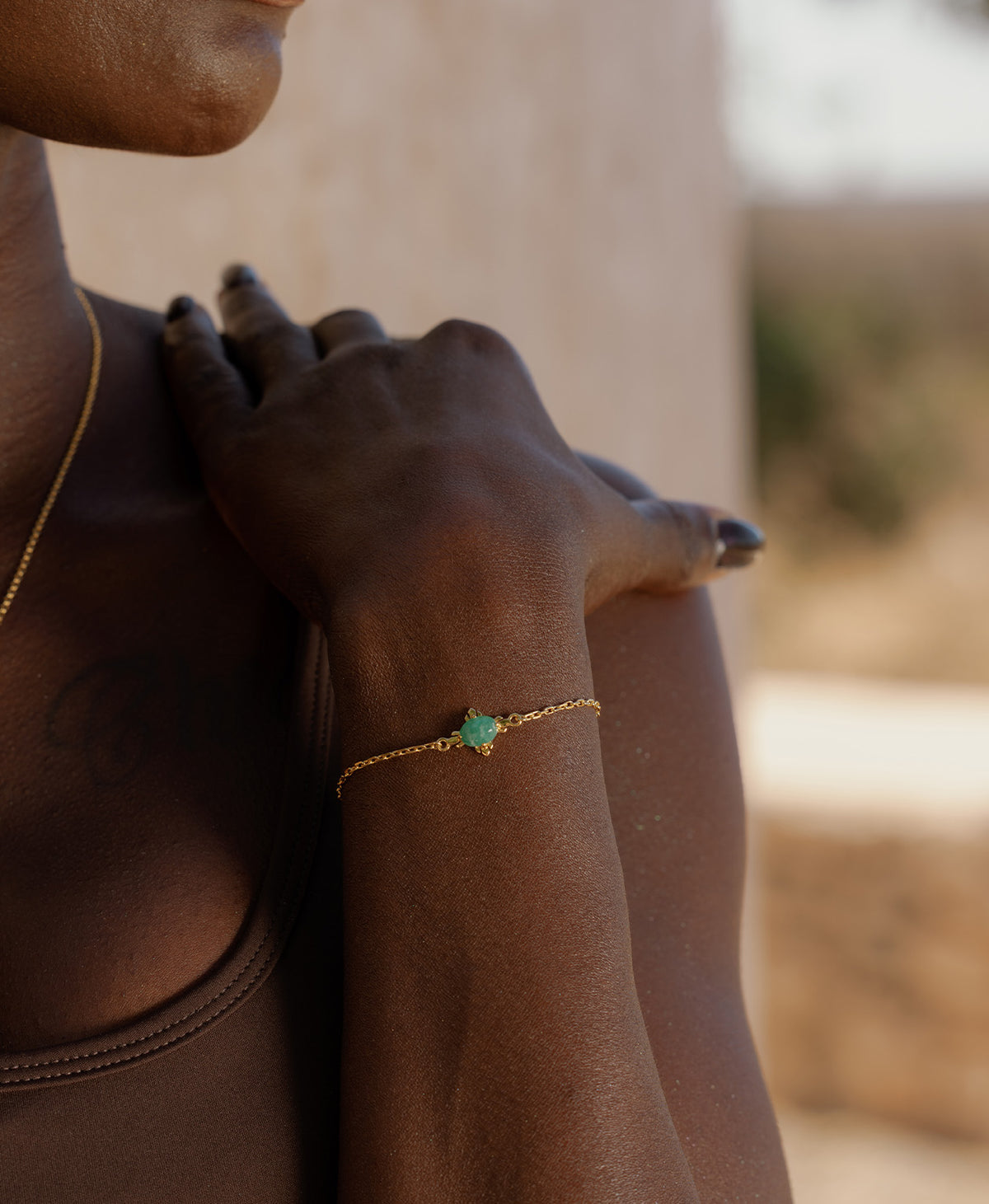 A close-up of a wrist wearing the Farah Bracelet, a gold pendant with a cabochon cut emerald, set on a fine cable chain.