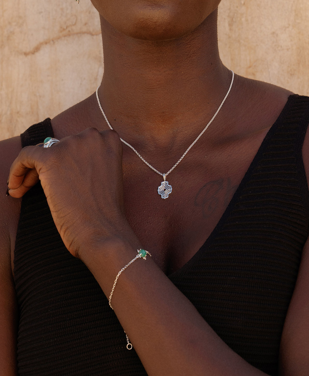 A close-up of a wrist wearing the Farah Bracelet, a silver pendant with a cabochon cut emerald, set on a fine cable chain, paired with a silver pendant necklace.
