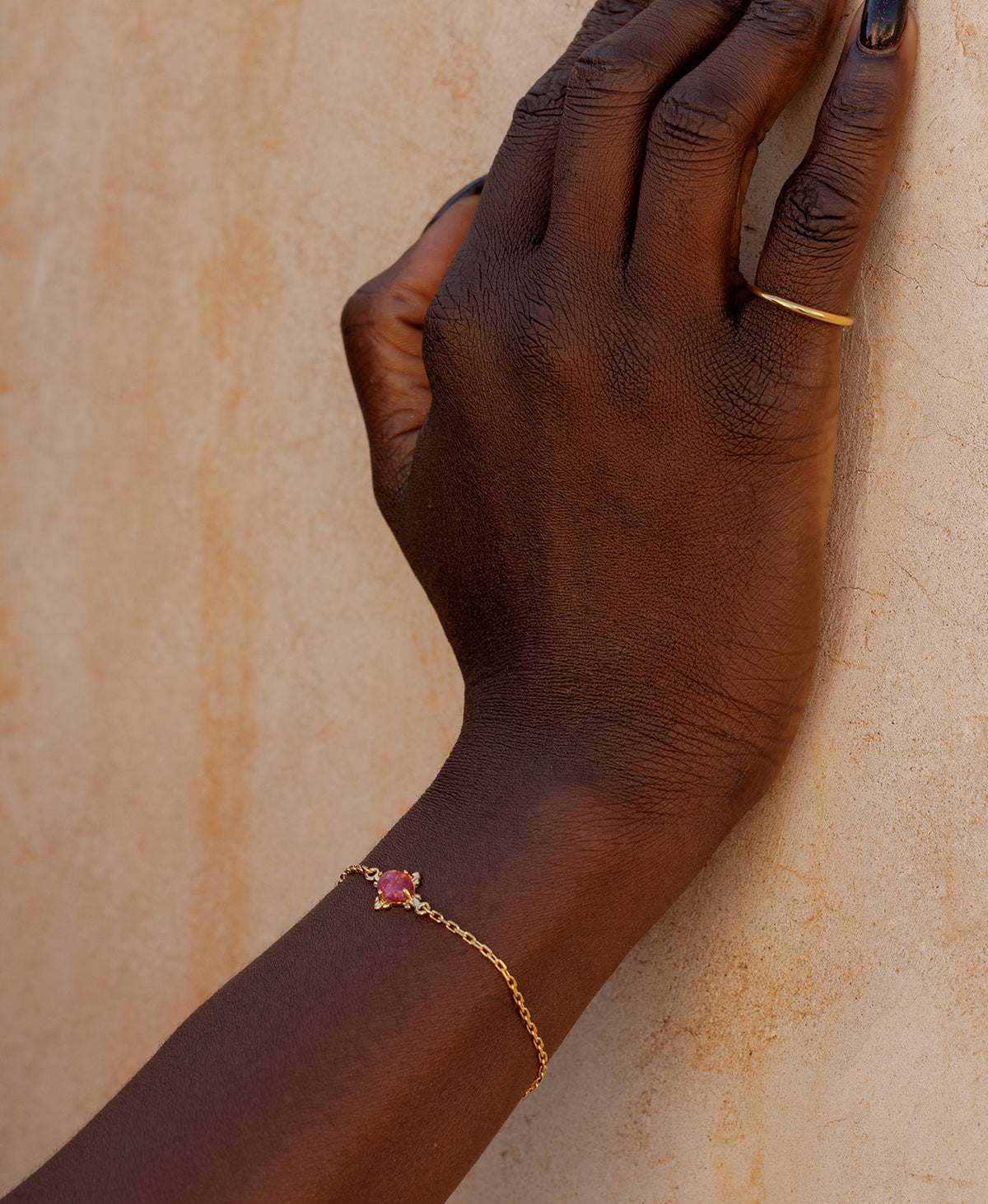 A close-up of a wrist wearing the Farah Bracelet, a gold pendant with a cabochon cut pink tourmaline, set on a fine cable chain.