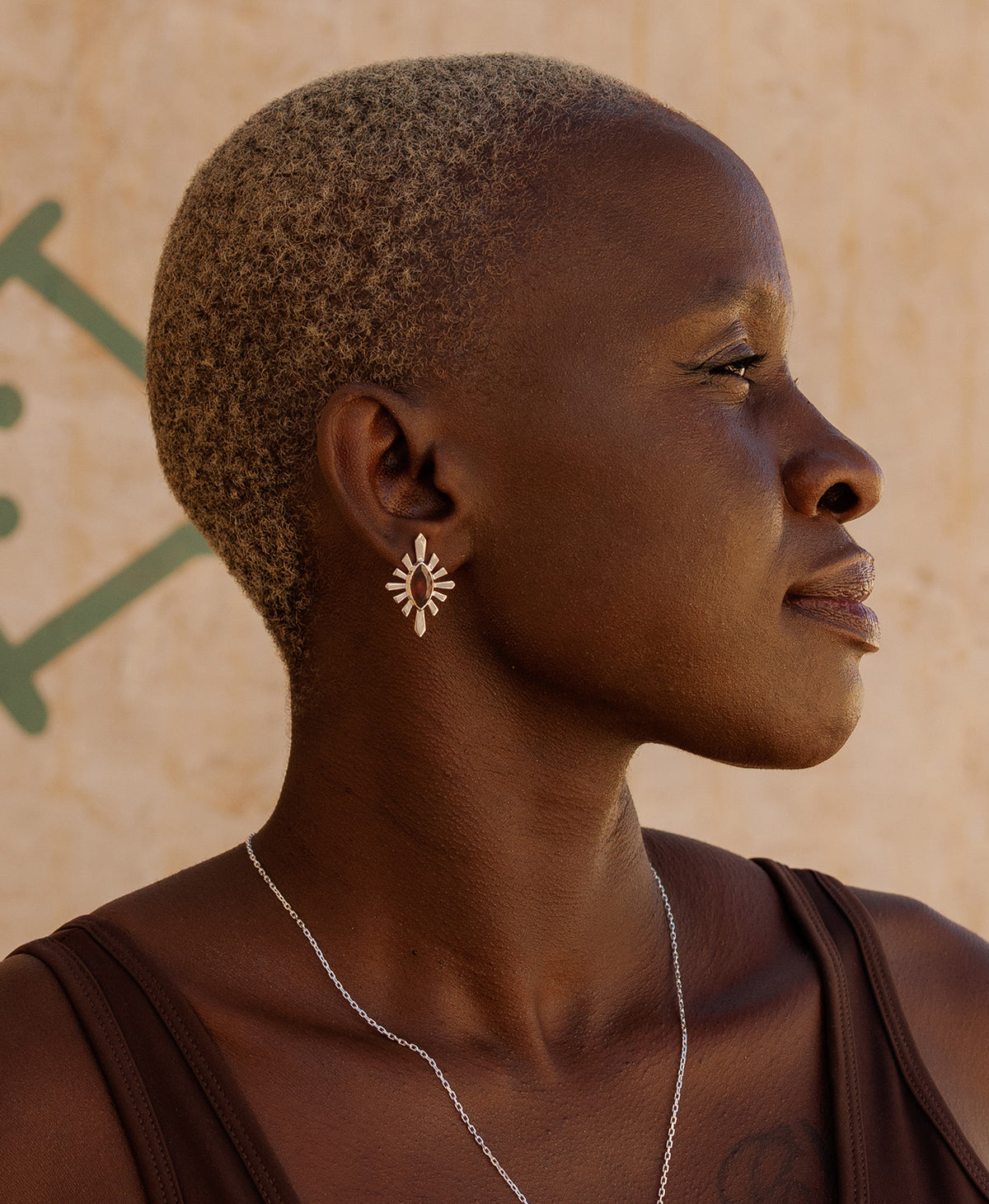 A side profile of a person wearing the Sister Studs, featuring a marquise cut garnet in a silver linear sunburst frame.
