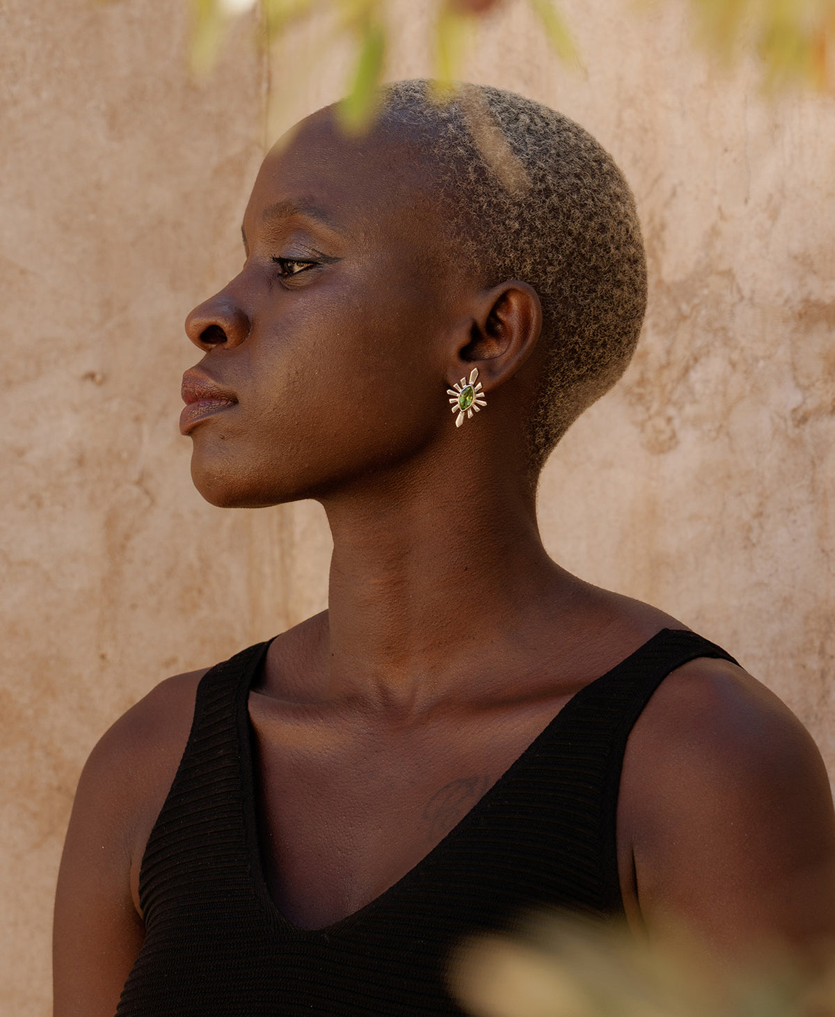 A side profile of a person wearing the Sister Studs, featuring a marquise cut peridot in a silver linear sunburst frame.