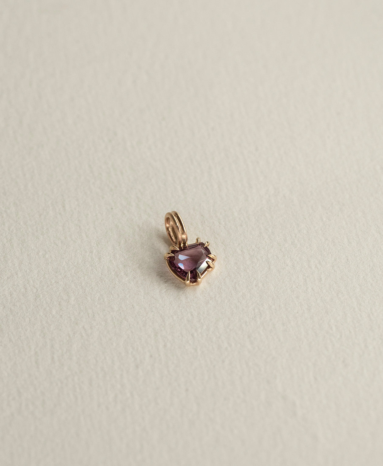 Angled view of the One of a Kind Charm 507 in 9k Yellow Gold with a deep purple portrait cut Sapphire.