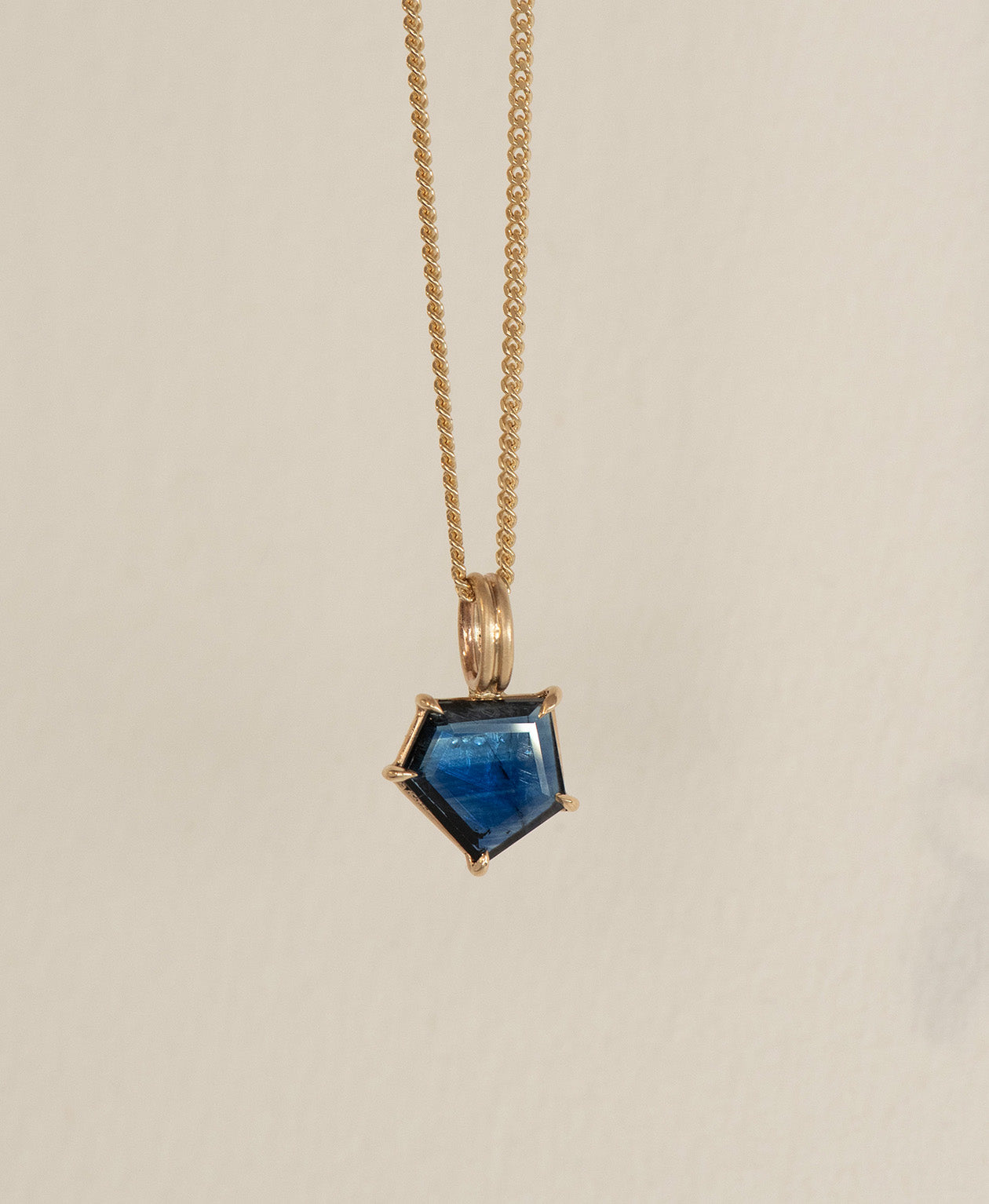 Close up of the One of a Kind Charm 508 with a deep blue portrait cut Sapphire on a curb chain.