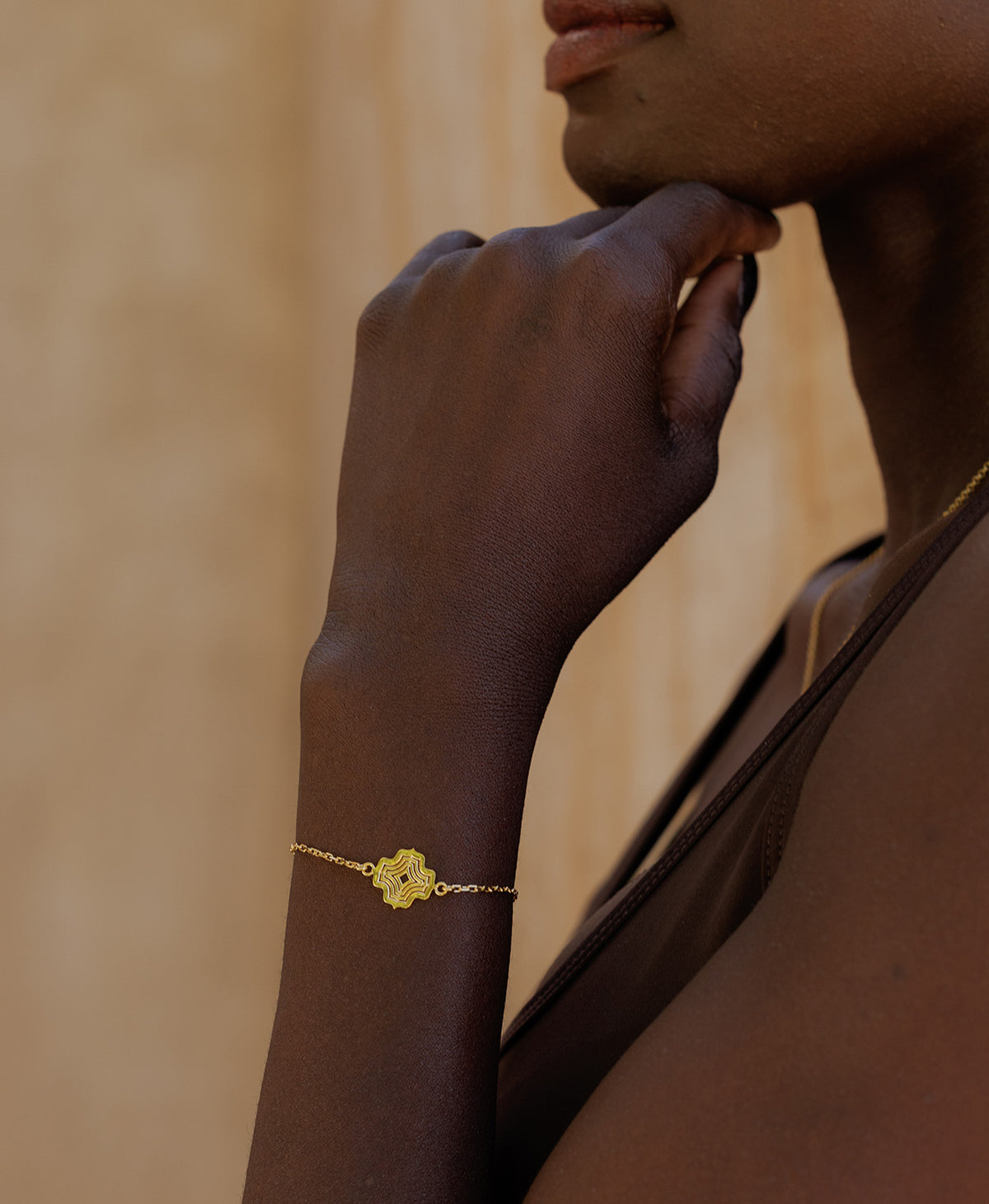 A close-up of an arm wearing the Alma Bracelet, a gold pendant with a concentric wave design set on a fine cable chain.