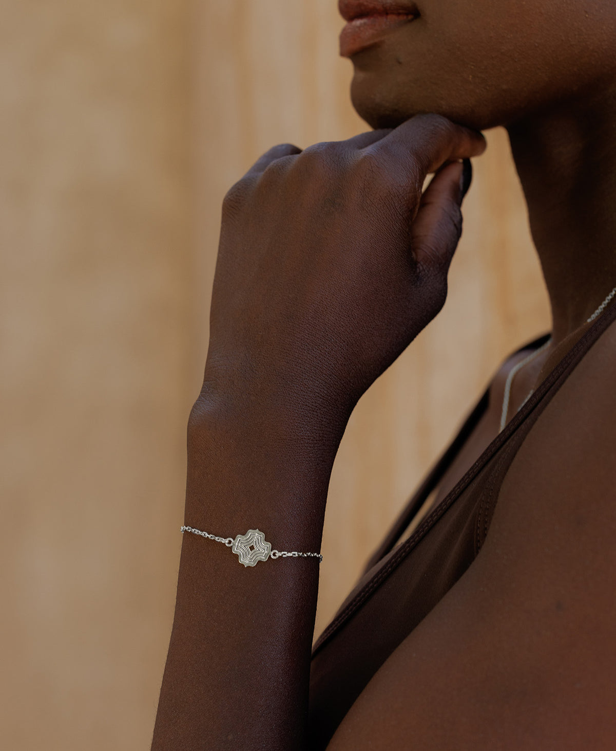A close-up of an arm wearing the Alma Bracelet, a silver pendant with a concentric wave design set on a fine cable chain.