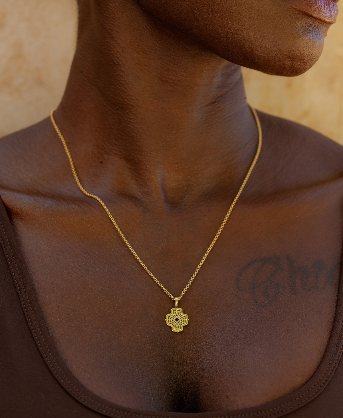 A close-up of a neck wearing the Nora Necklace, a gold pendant with a concentric wave design, suspended from a fine belcher chain.