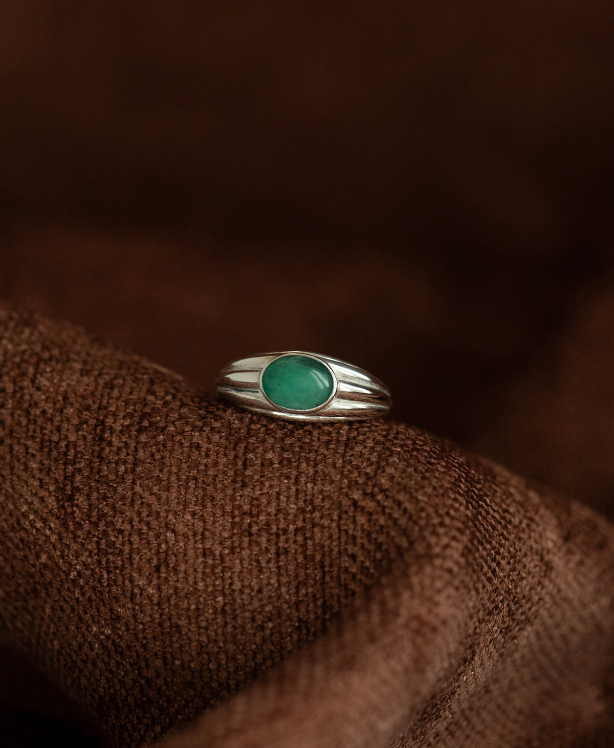 The silver Esmeralda Ring, featuring a cabochon cut Emerald set in a graduated band, rests on a textured brown background. 