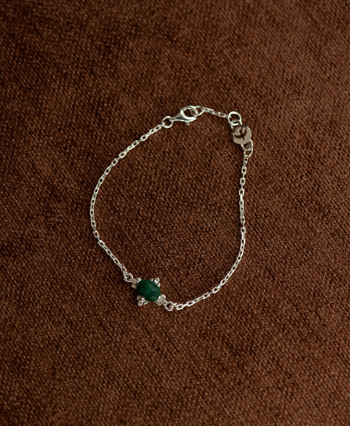 The silver Farah Bracelet featuring a cabochon cut emerald, on a textured brown fabric background.