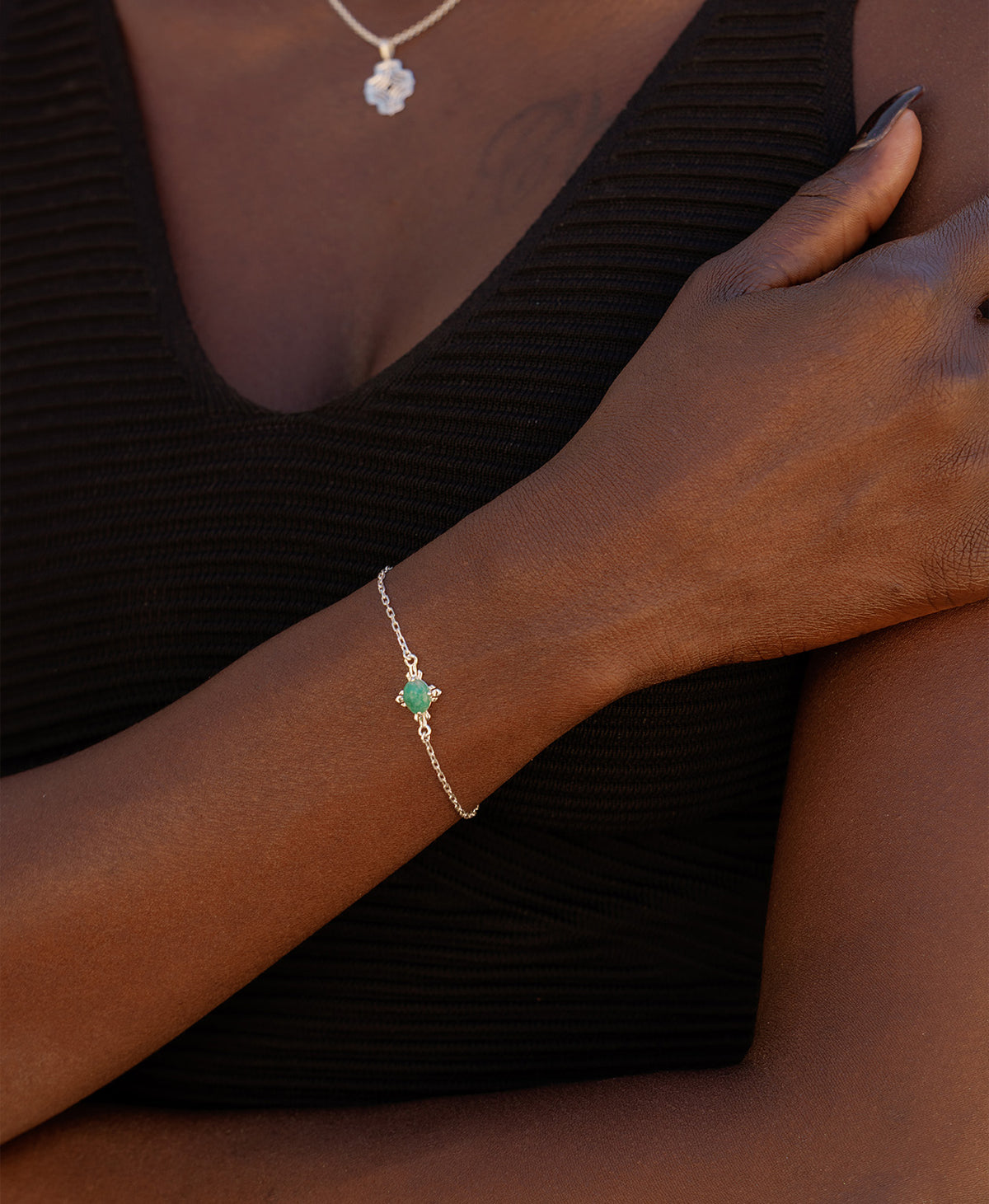 A close-up of a wrist wearing the Farah Bracelet, a silver pendant with a cabochon cut emerald, set on a fine cable chain.