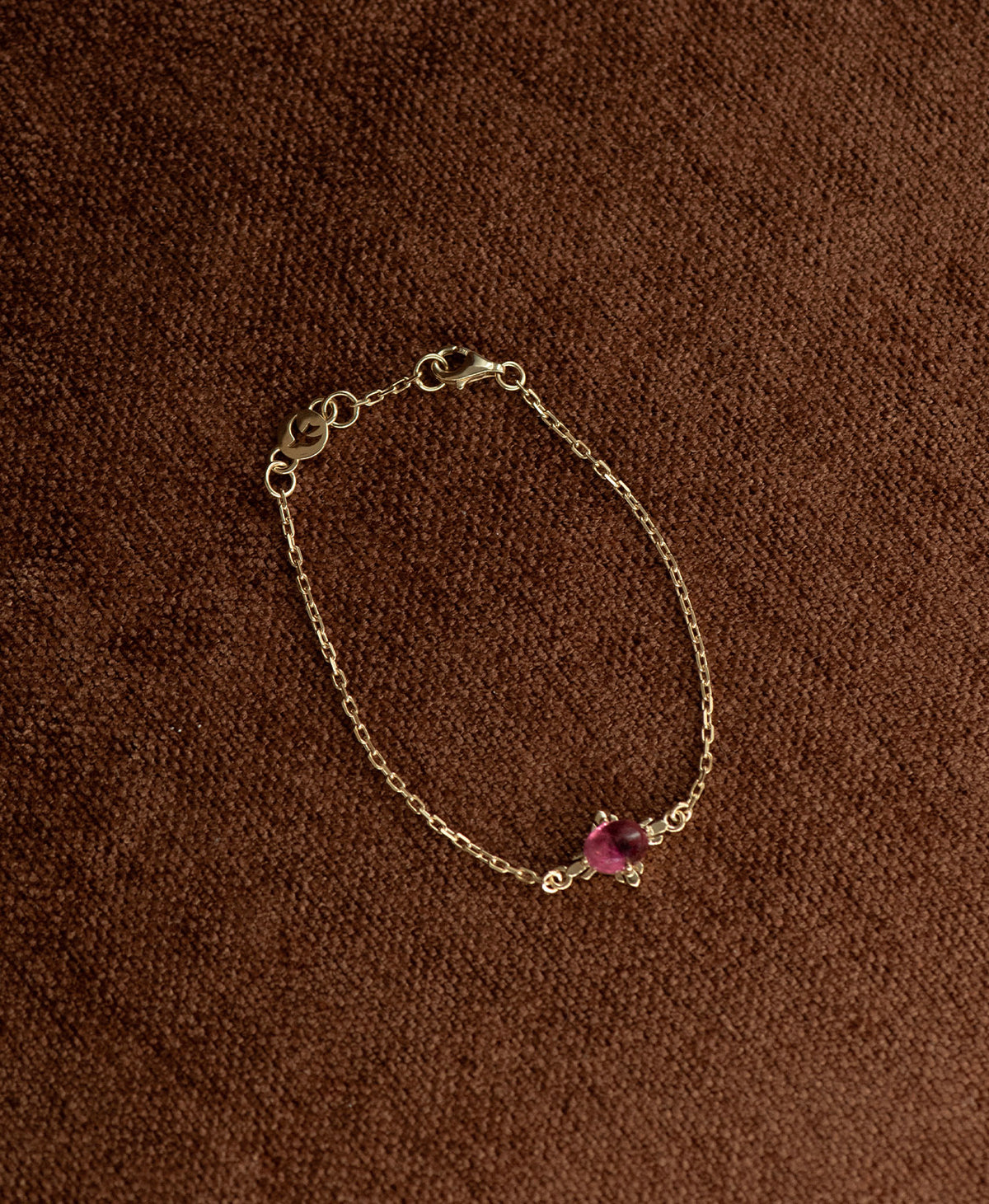 The gold Farah Bracelet featuring a cabochon cut pink tourmaline, layered over a cream stone on a textured brown fabric background.
