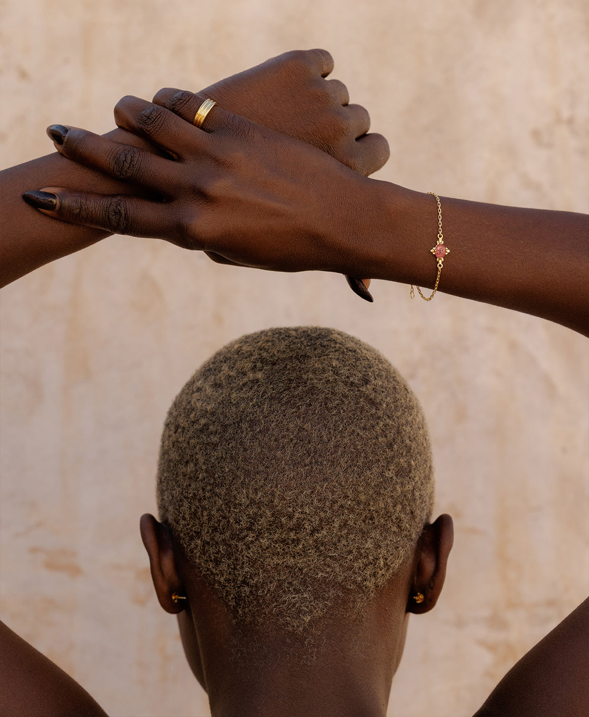 A close-up of a person wearing the Farah Bracelet, a gold pendant with a cabochon cut pink tourmaline paired with a gold pinky ring. 