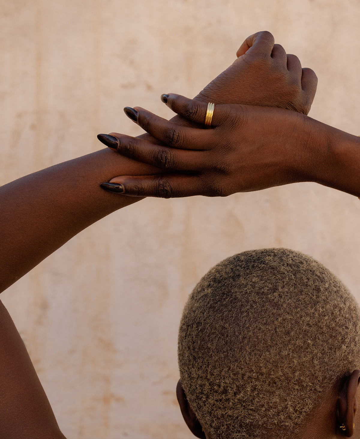 A closeup of a hand and arm, wearing the gold Irma Stacker Ring, formed from three connected bands, layered closely.