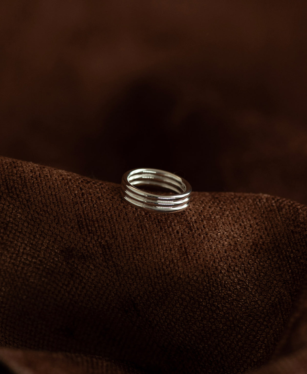 The silver Irma Stacker Ring, formed from three connected bands, layered closely, rests on a textured brown background.