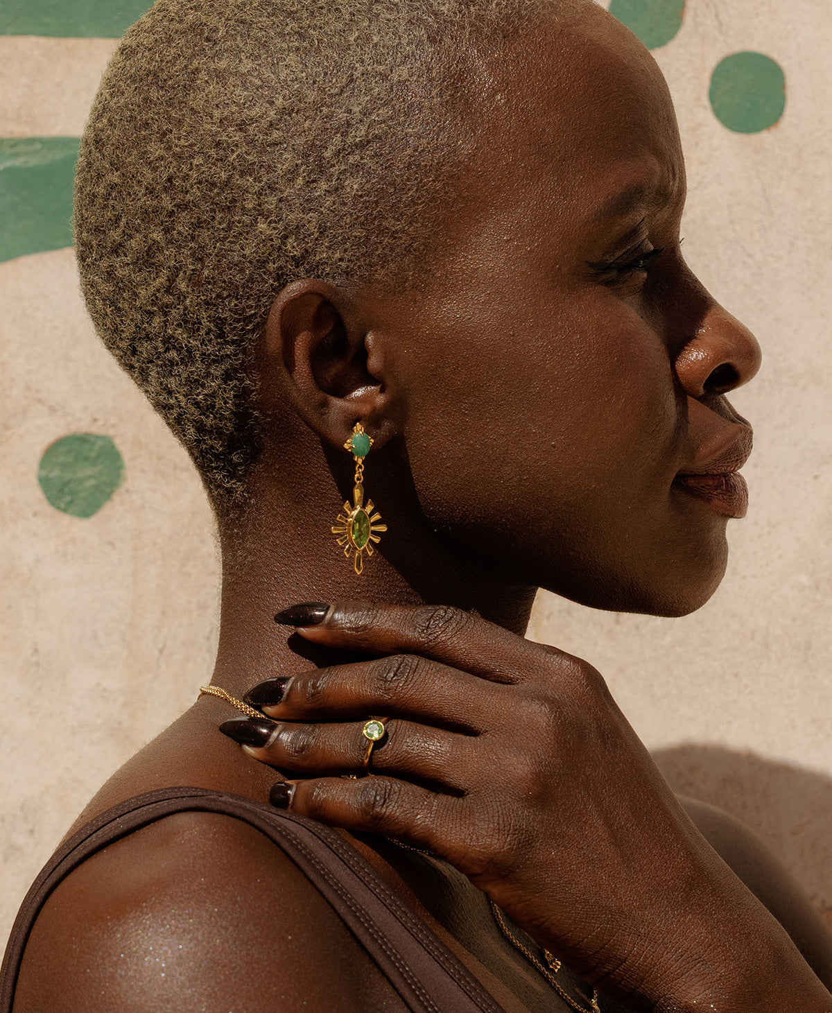 A close up of a woman wearing the gold Mon Petit ring in peridot on her ring finer paired with long gold peridot earrings. 