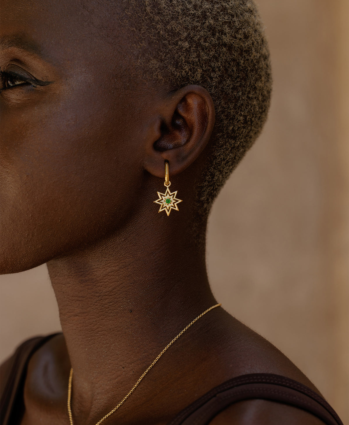A close-up side profile of a person wearing the Nora Hoops, featuring a gold star hanging from a hoop with a central green stone.