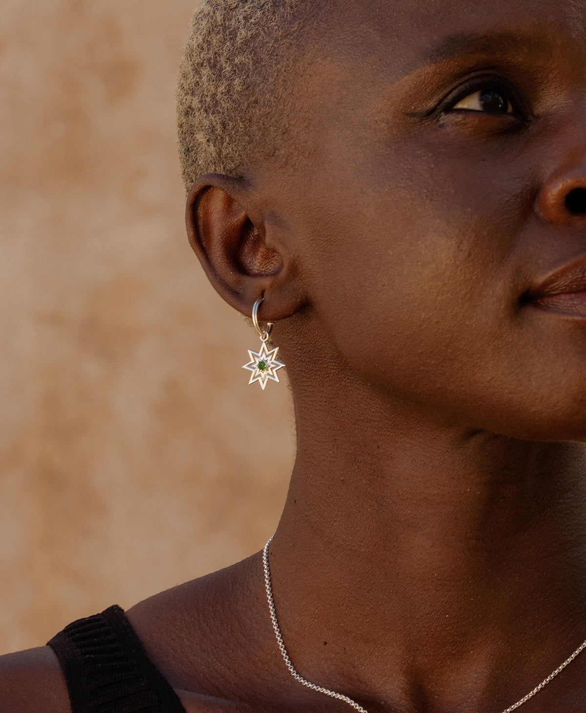 A close-up side profile of a person wearing the silver Nora Hoops, featuring a gold star hanging from a hoop with a central green stone.