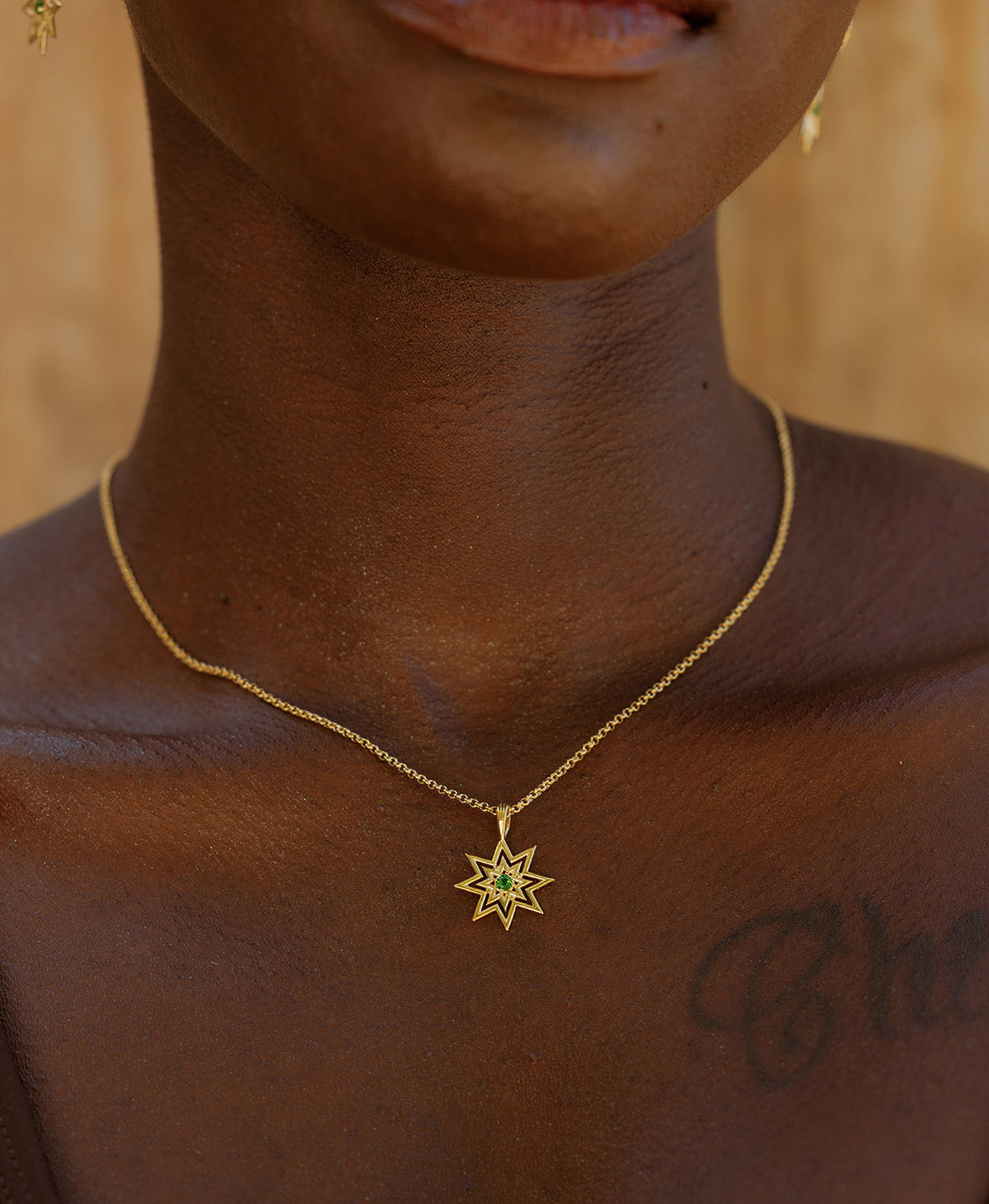 A close-up of a neck wearing the Nora Necklace, a gold eight pointed star pendant with a central green stone. 
