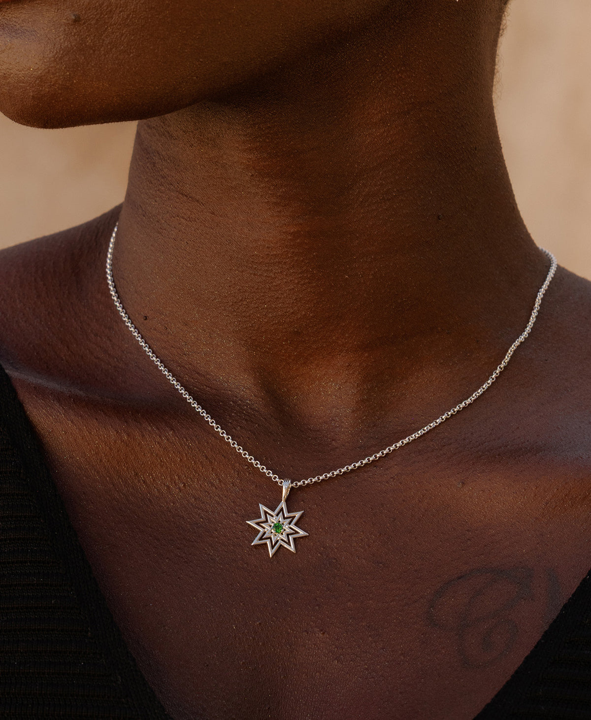 A close-up of a neck wearing the Nora Necklace, a silver eight pointed star pendant with a central green stone. 