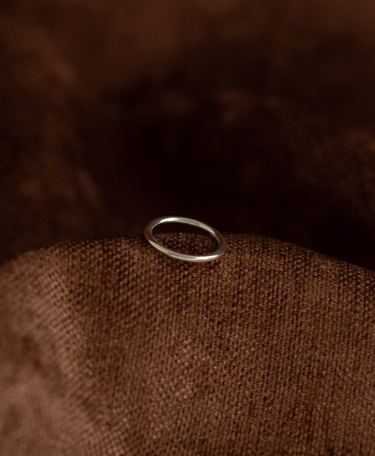 The smooth, curved Selma stacking ring in 925 sterling silver, rests on a textured brown background. 