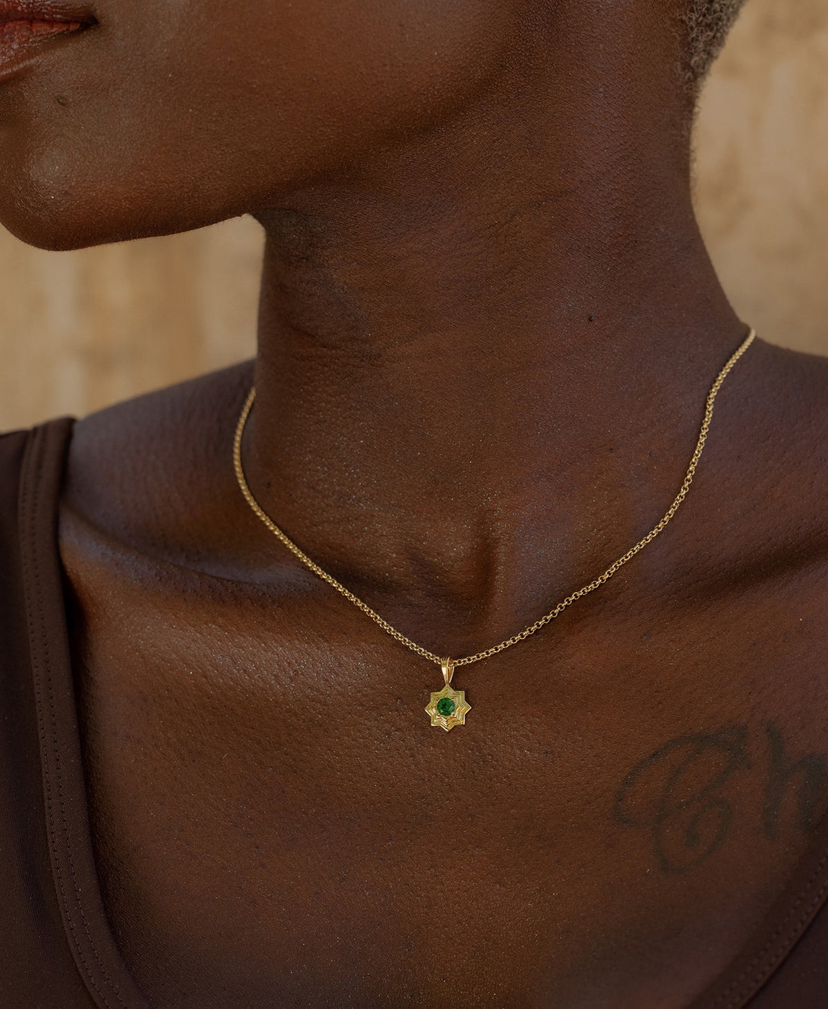 A close-up of a neck wearing the Sitara Necklace, a gold star-like pendant with a central green stone. 