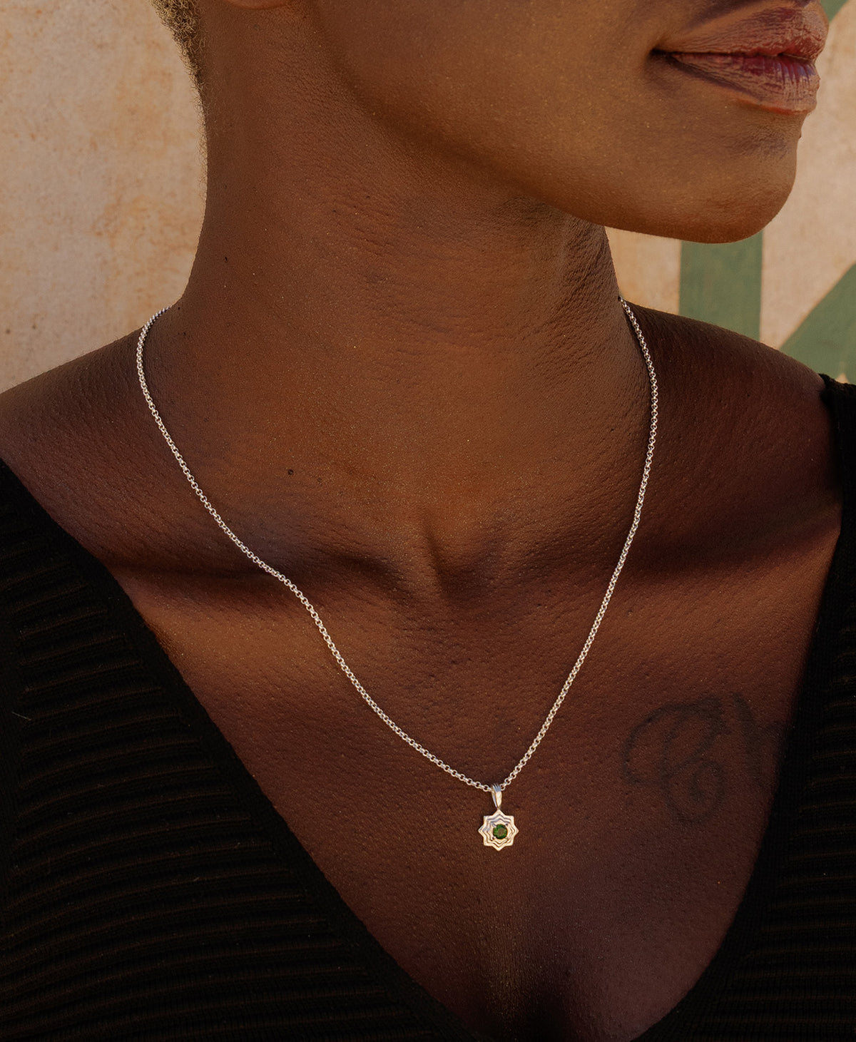 A close-up of a neck wearing the Sitara Necklace, a silver star-like pendant with a central green stone. 
