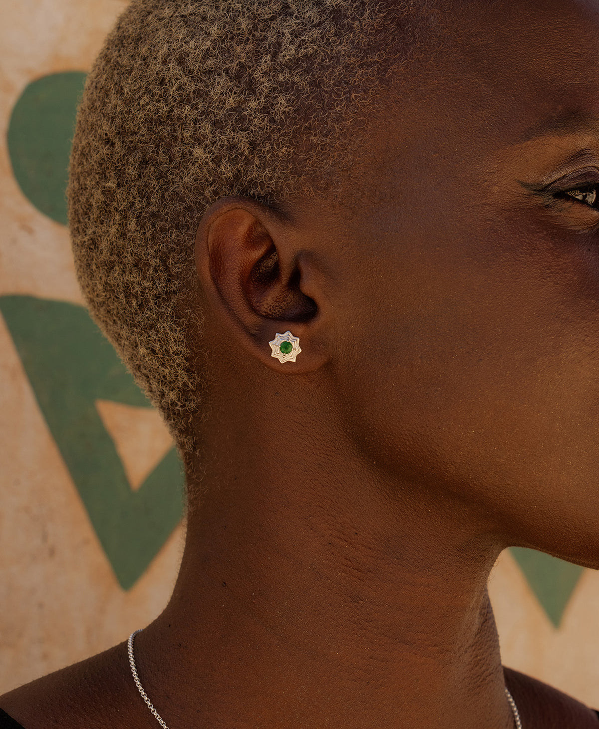 A close-up side profile of a person wearing the Sitara Studs, a silver star-like stud with a central green stone. 