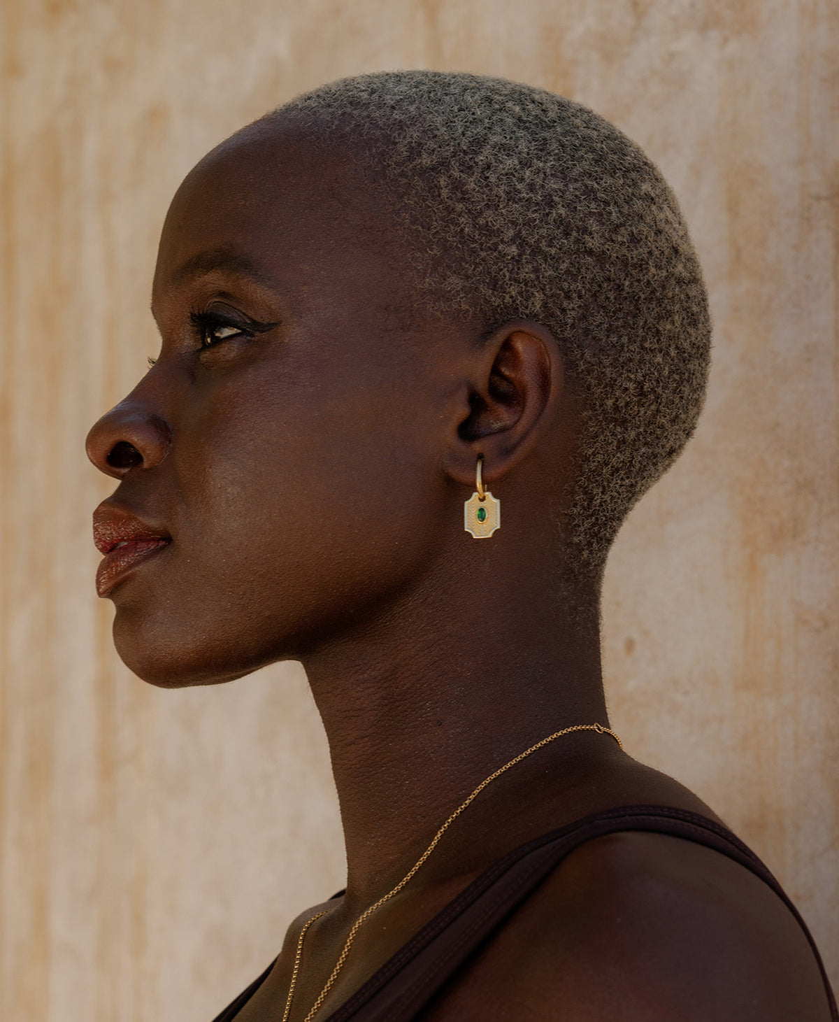 A close-up of a person wearing the Soul Sister Hoops, featuring a textured gold pendant with a central green stone on a hoop.